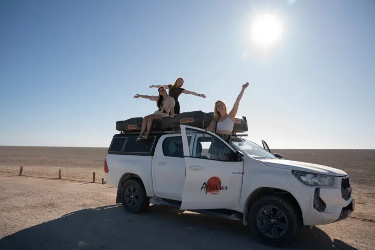 three women posing on a white safari truck in a desert landscape