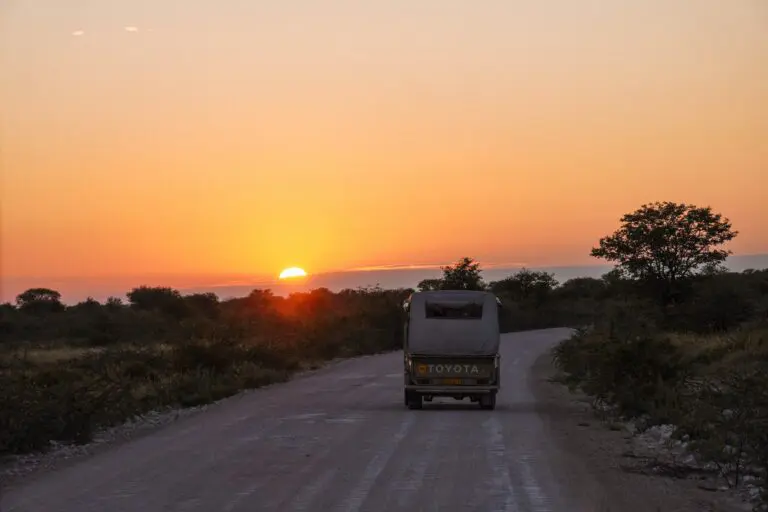 safari vehicle driving on dirt road at sunset in Namibia