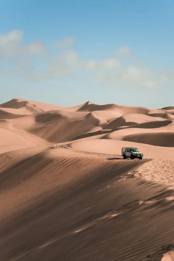 white 4x4 vehicle driving on sand dunes in Namibia