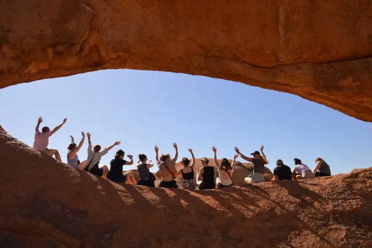 group of people waving under a natural rock arch in Namibia
