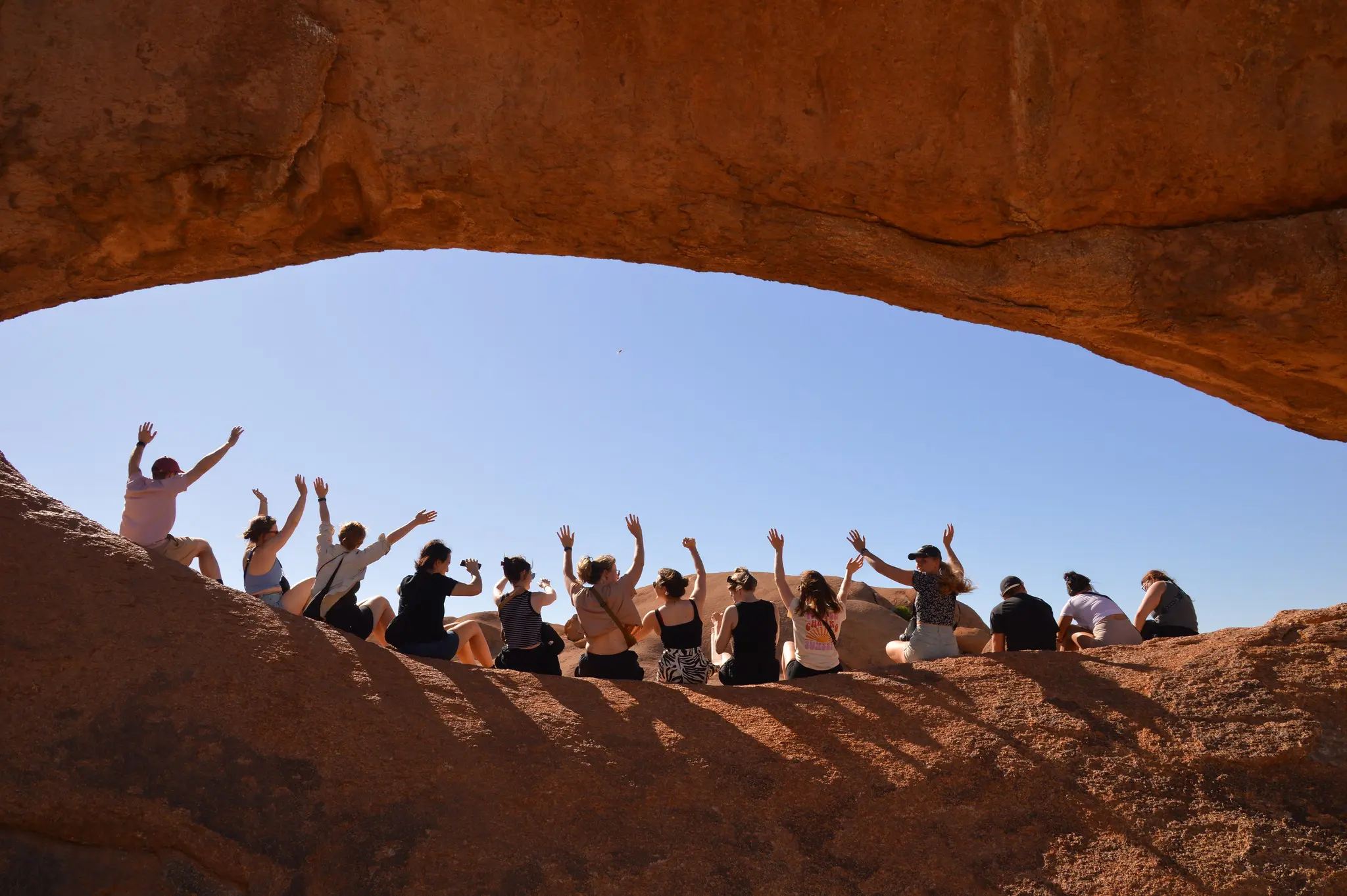 group of people waving under a natural rock arch in Namibia