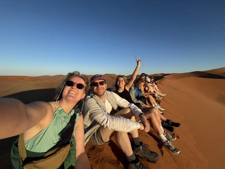 group of friends taking a selfie on a desert dune at sunset
