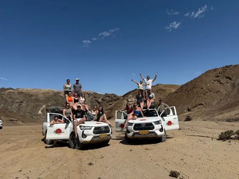 group of friends posing on safari vehicles in namibian desert