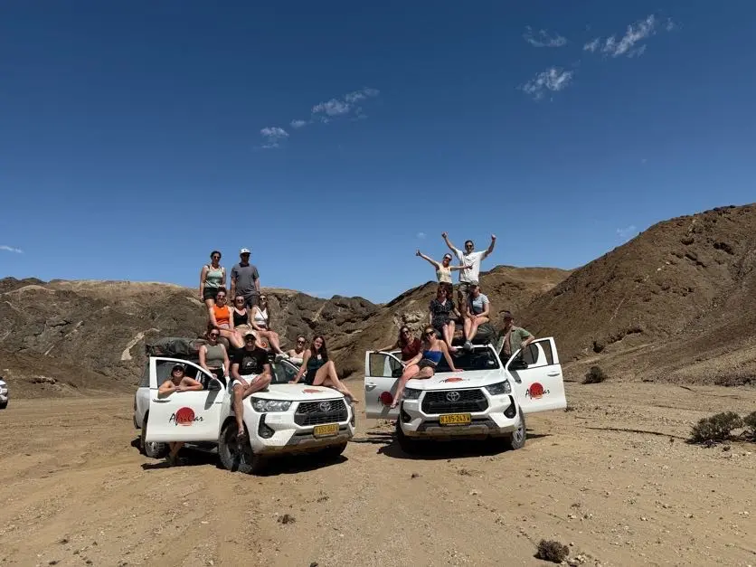 group of friends posing on safari vehicles in namibian desert