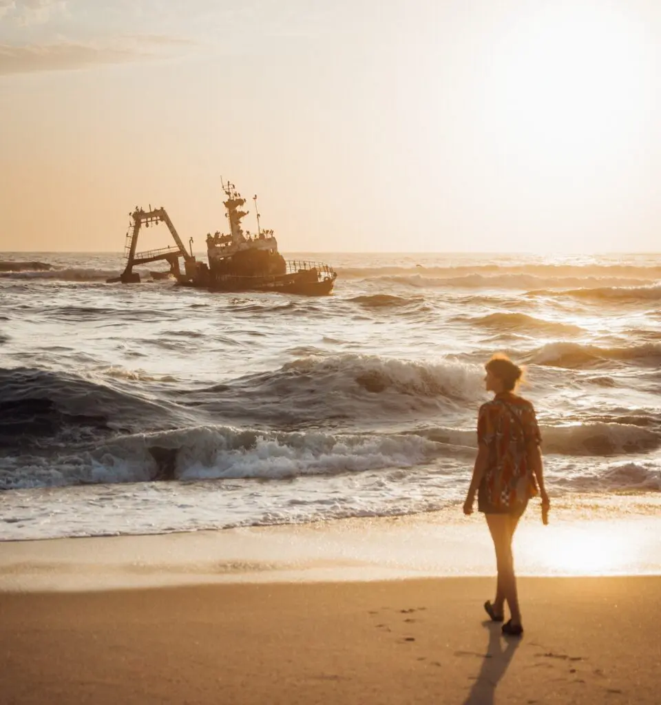 woman walking on beach towards shipwreck at sunset in Namibia