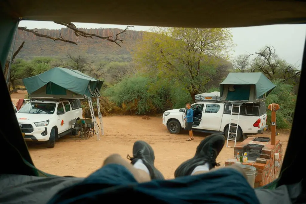 person relaxing in rooftop tent at campsite in Namibia