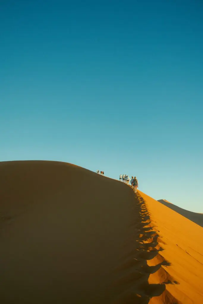 group of people hiking up a sand dune in Namibia