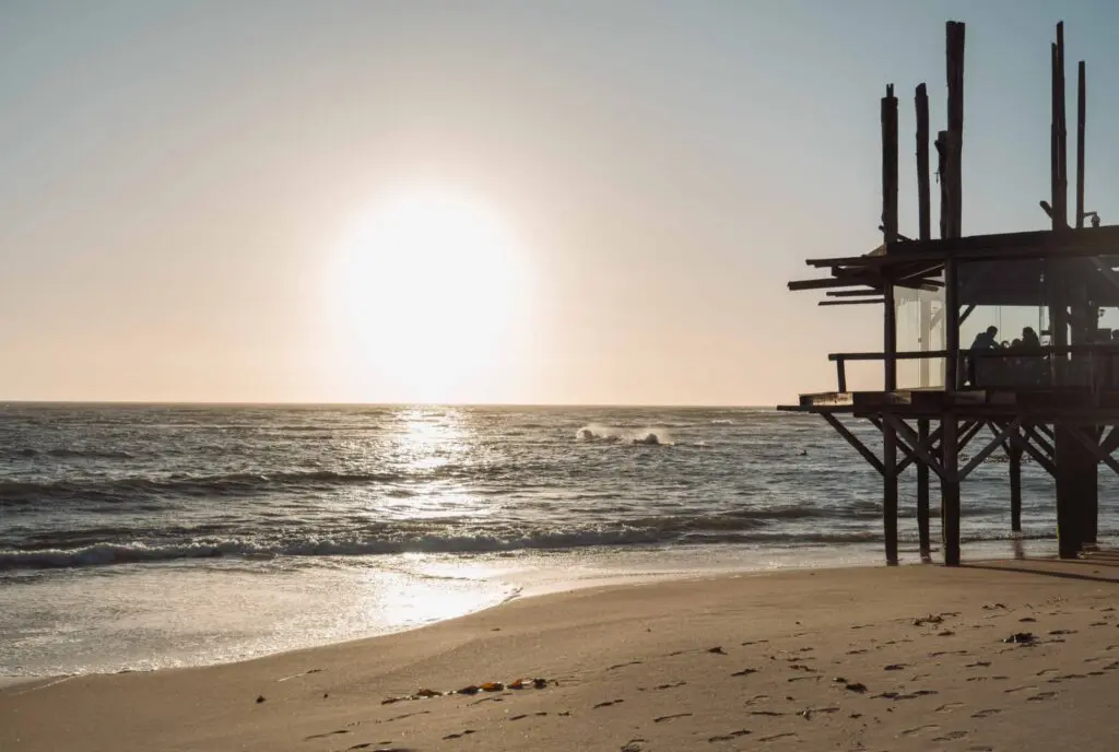 sunset over the ocean with a wooden stilt structure on the beach