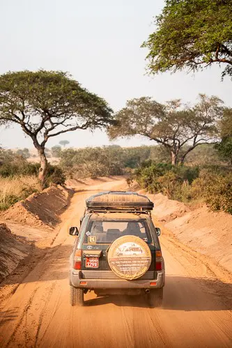 safari vehicle driving on a dusty red dirt road in Uganda