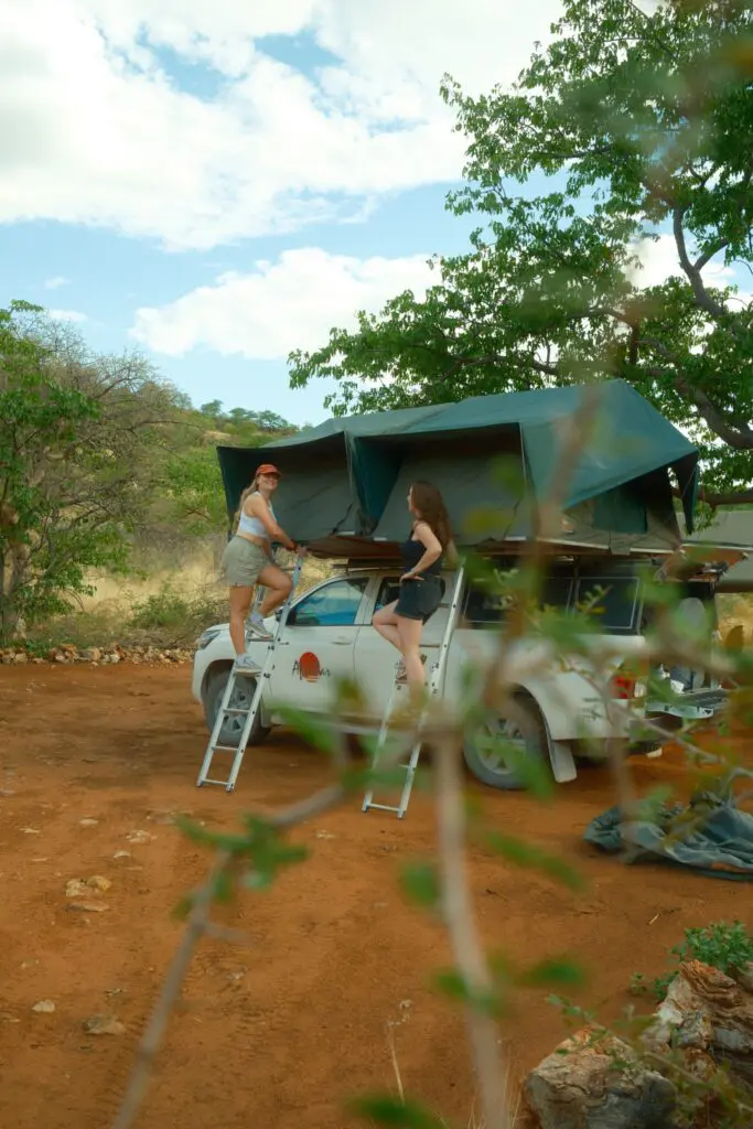 two women climbing ladders to rooftop tents on a safari truck