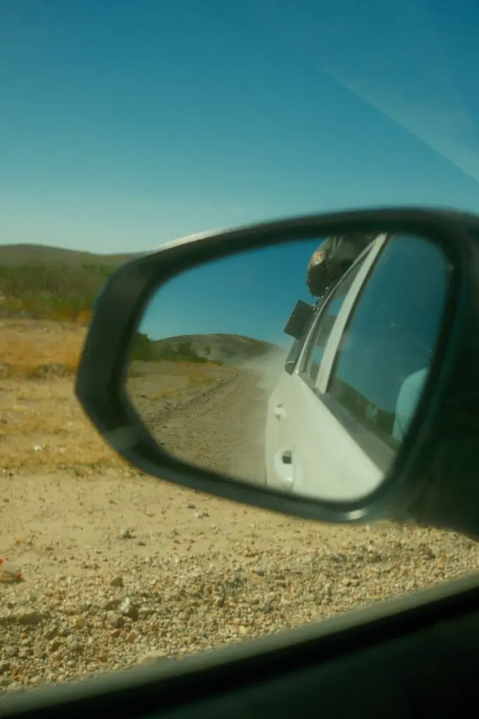 car driving on a dusty road in Namibia, seen through a side mirror