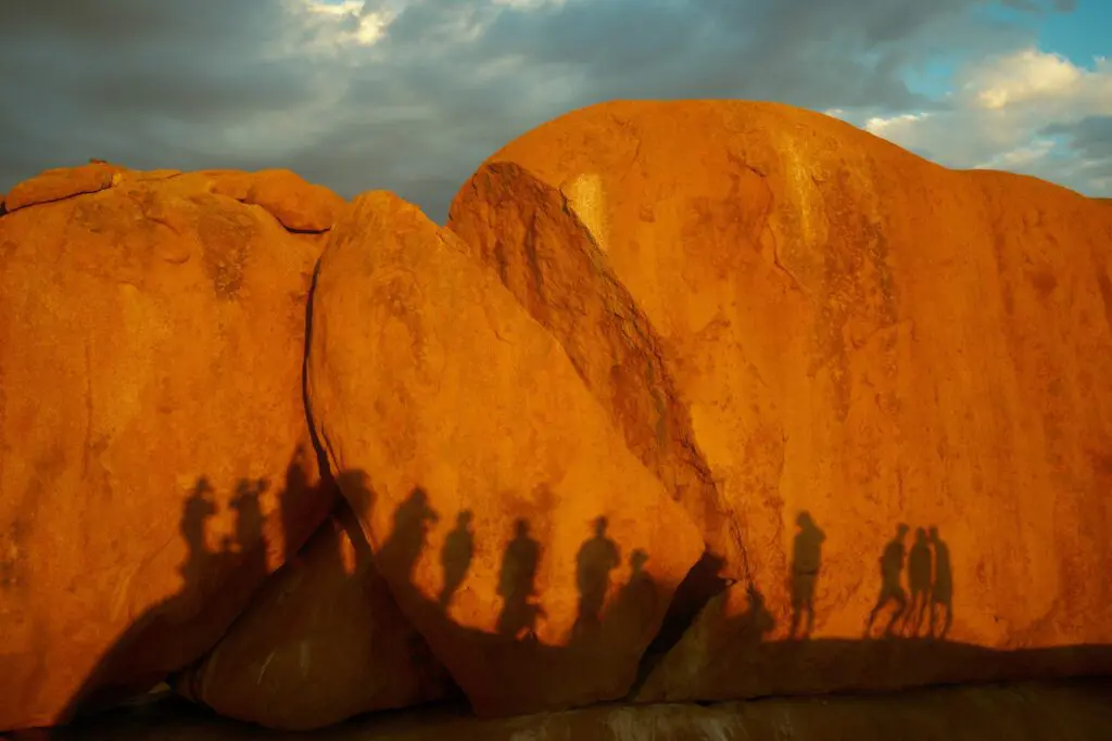 long shadows of people on orange rock formations at sunset