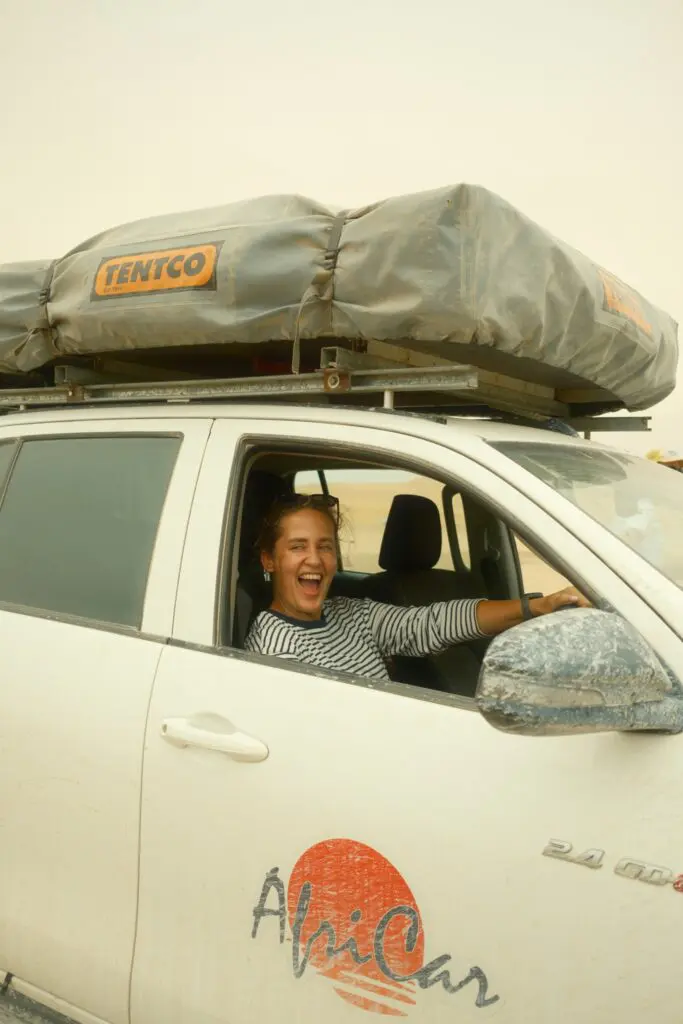 woman laughing in a white 4x4 with rooftop tent in Namibia