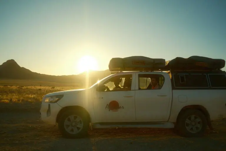 white pickup truck with rooftop tents driving in namibian desert at sunset