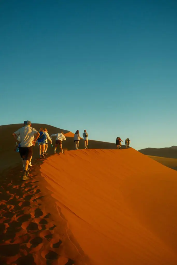 group of people hiking up a red sand dune in Namibia