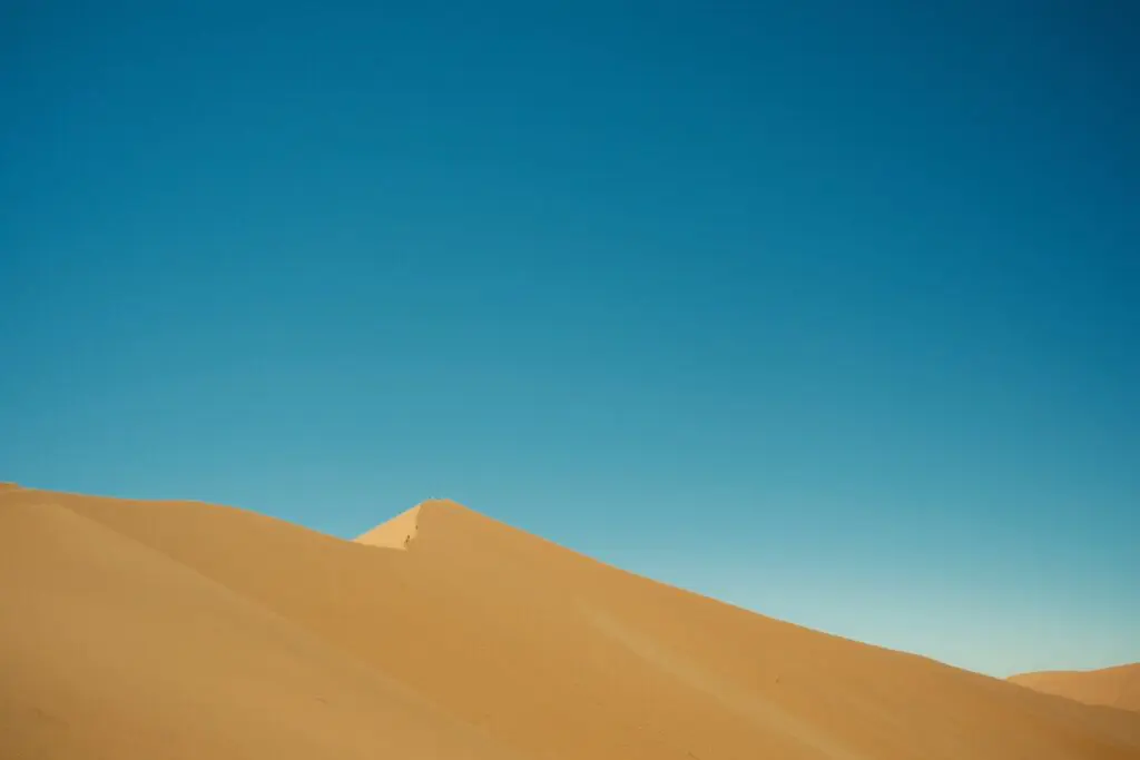 tiny people hiking up a vast sand dune in Namibia