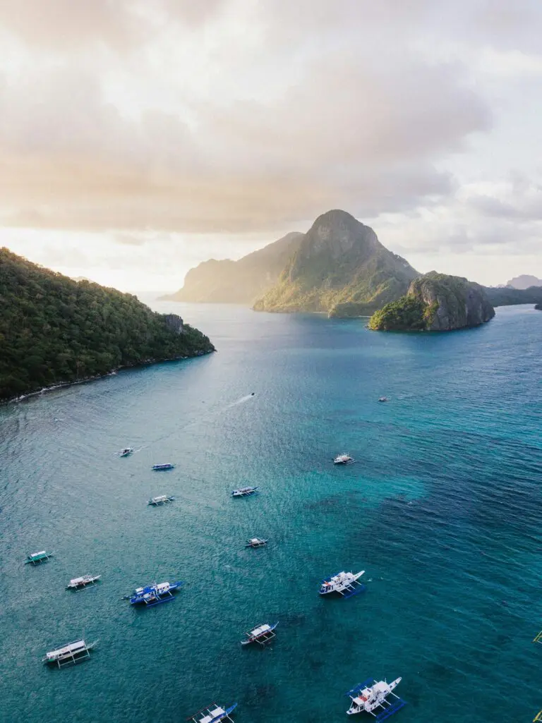 drone shot of boats in clear blue water with islands at sunset