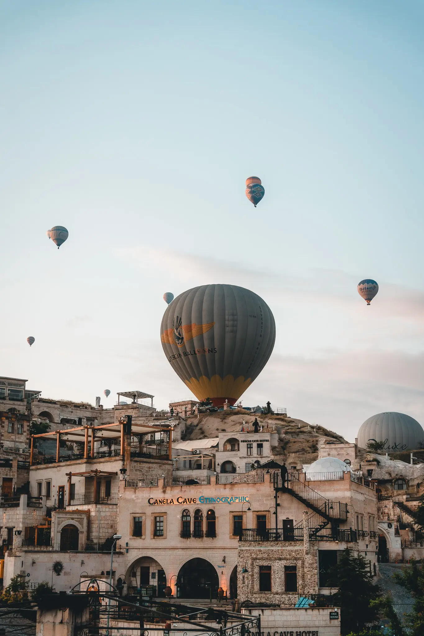 hot air balloons flying over a cave hotel village in Cappadocia