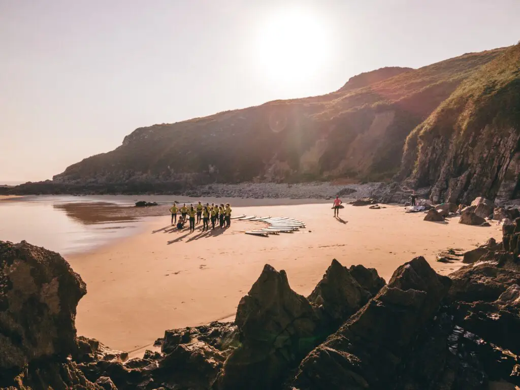 group of surfers on beach with surfboards at sunset
