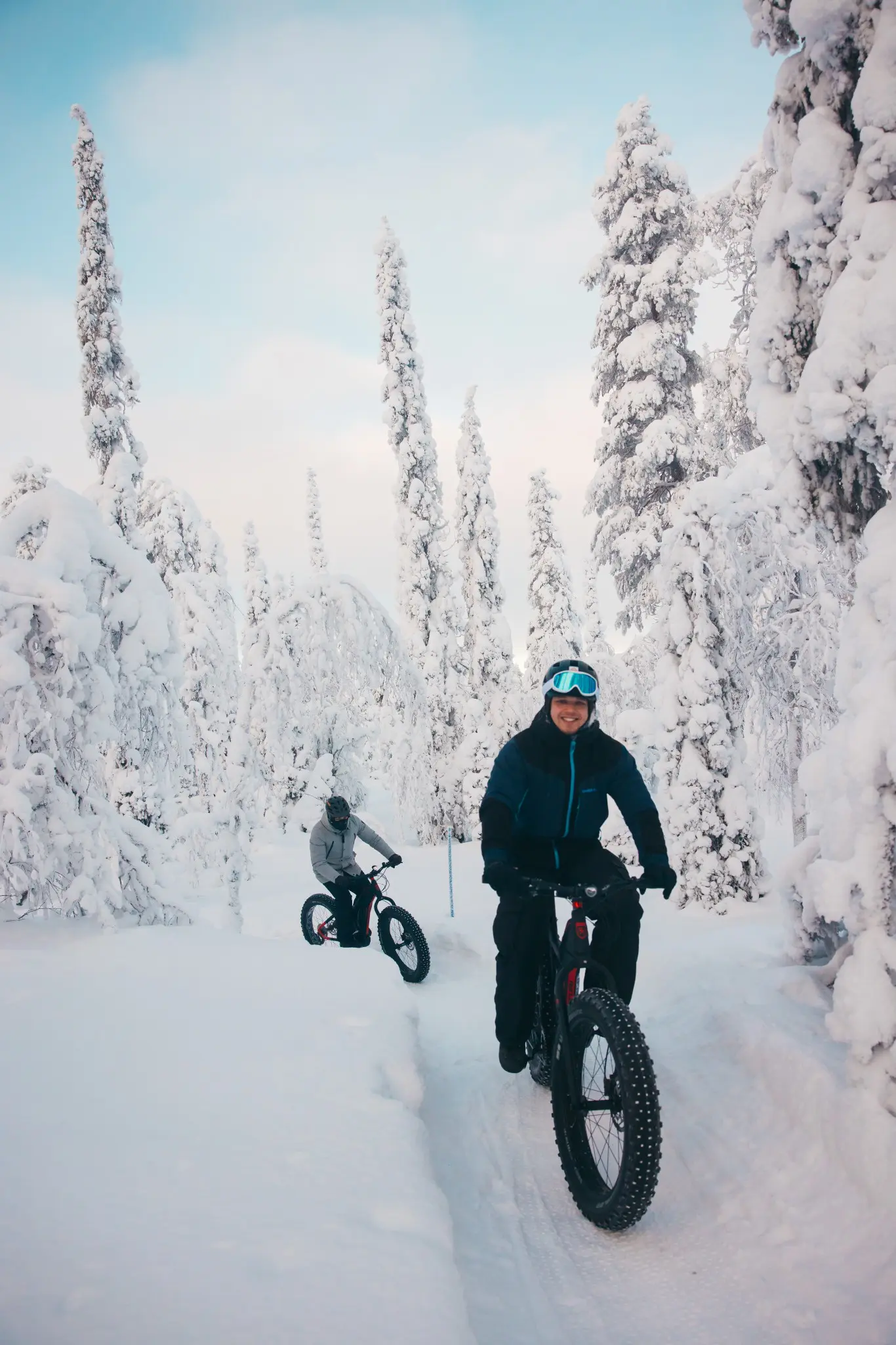 two people fat biking through a snowy forest in Lapland