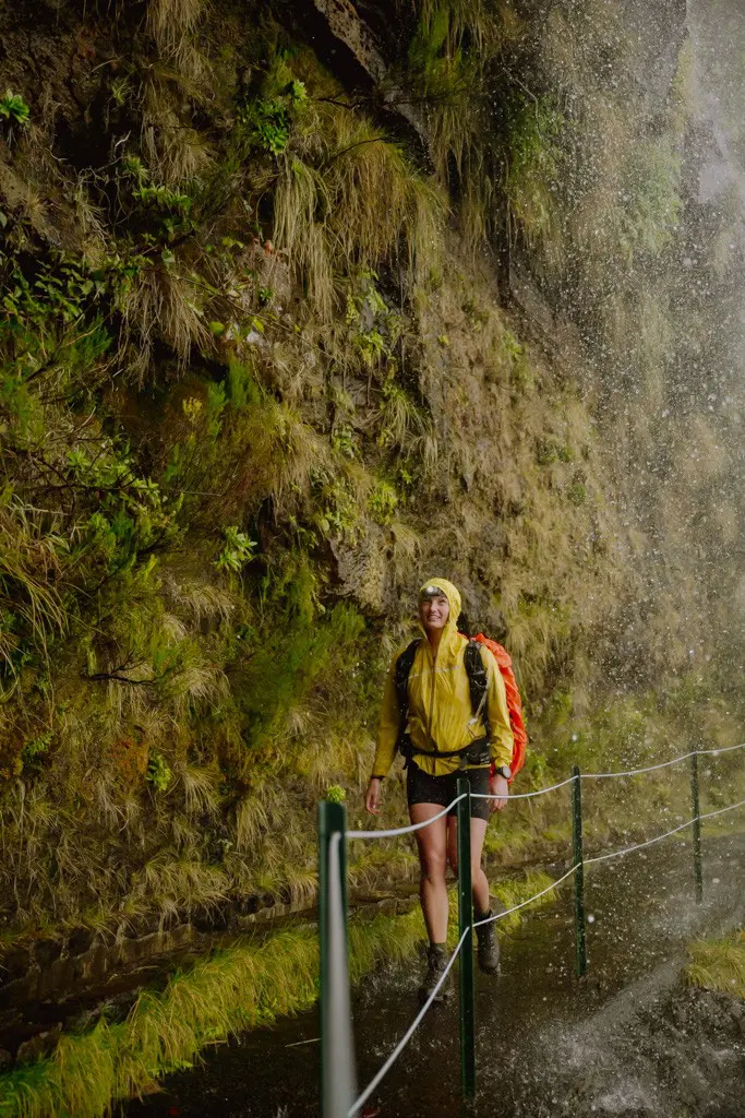 hiker in yellow jacket walking under waterfall on Madeira Trail