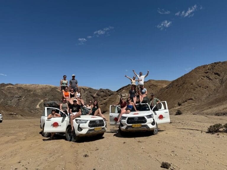 group of friends posing on safari vehicles in namibian desert